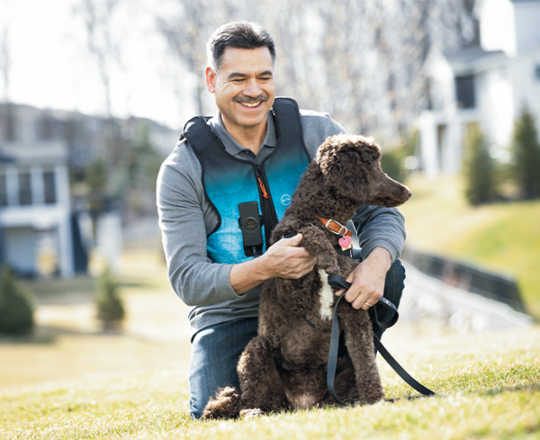 Man wearing a medical vest hugging dog outdoors and smiling