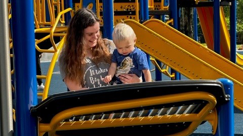 A mother holds her son on some playground equipment