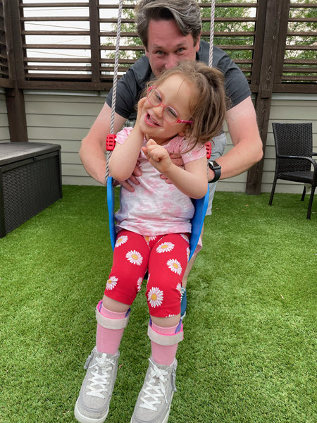 A father pushes his daughter on a swingset