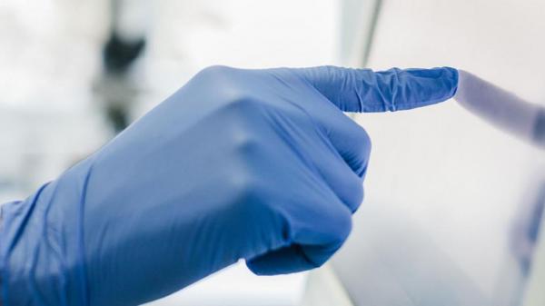 Image of hand with surgical glove touching a screen