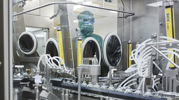 A manufacturing employee in a mask and gown looks over a bottling line