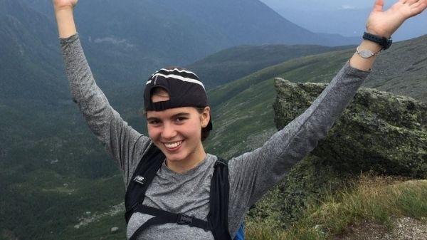 Young women shares her excitement with arms outstretched overlooking a valley below