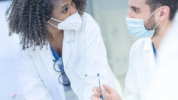 Two masked clinicians confer in a hospital setting