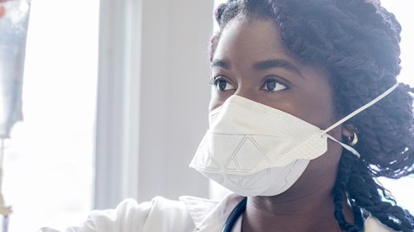 A nurse in a mask looks at an IV bag