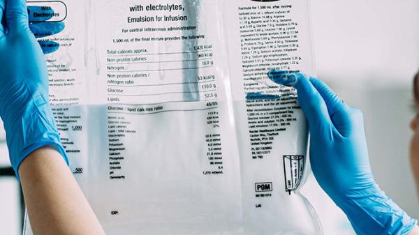 A healthcare professional wearing medical gloves looks at an IV bag