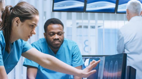 Nurses and technicians read a computer monitor