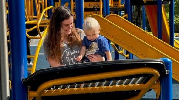 A mother holds her son on some playground equipment