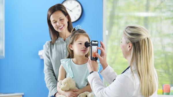A mother stands behind her child while a pediatrician does an eye exam