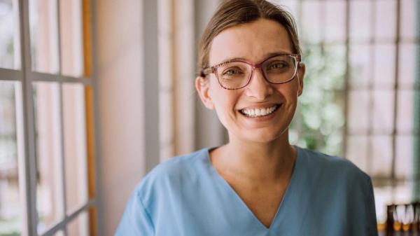 nurse smiling and standing next to a window 