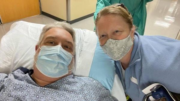 Baxter employee masked laying on a bed, wife crouched down beside him