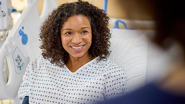 A patient in a med-surg bed smiles and talks to her clinician
