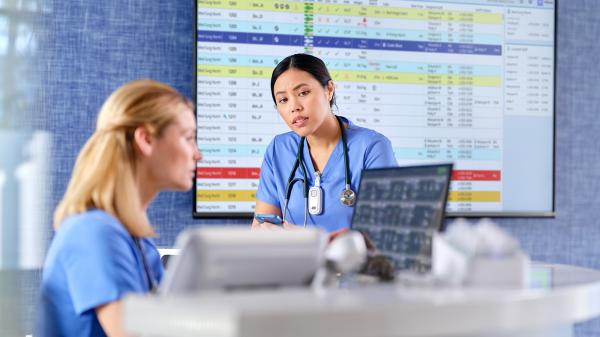 Clinicians review data on a monitor at a nurse’s station with a dashboard in the background