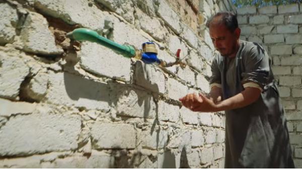 Man washes his hands from a faucet outside