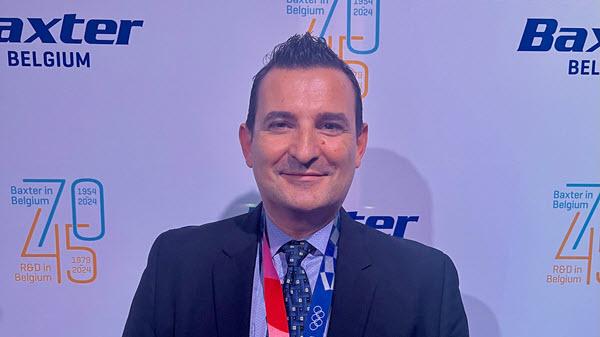 Baxter leader dressed in a suit and tie stands in front of a background with Baxter on it