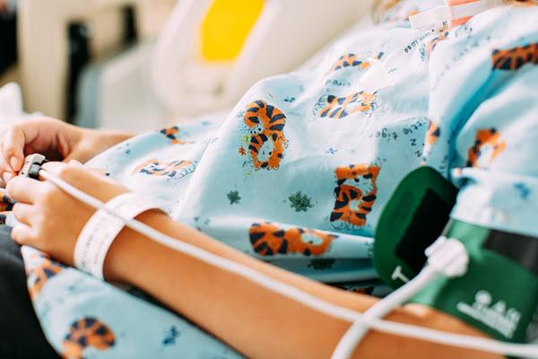 A child pictured from just upper torso rests in a hospital setting while connected to medical devices