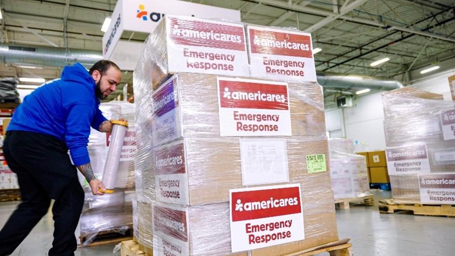 Americares employee uses plastic wrap to secure cardboard boxes.