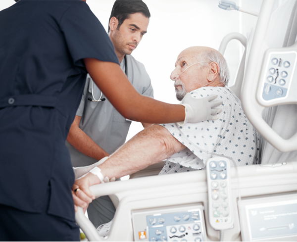 Two healthcare providers assisting a patient getting up from hospital bed