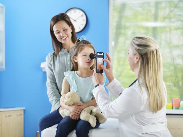 A mother stands behind her child while a pediatrician performs an eye exam