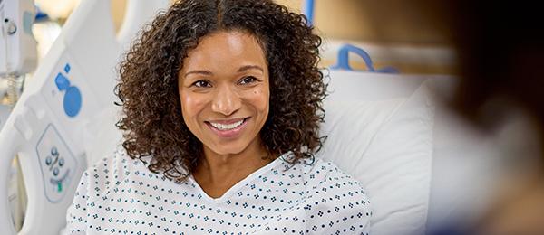 A patient in a med-surg bed smiles and talks to her clinician