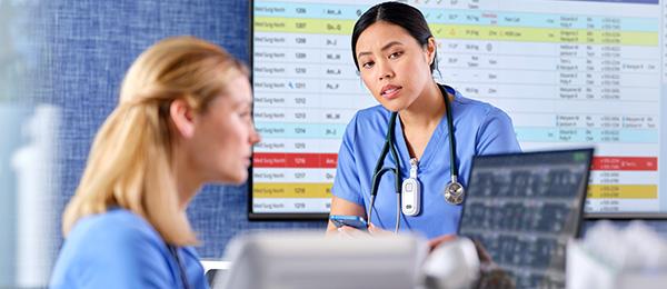 Clinicians review data on a monitor at a nurse’s station with a dashboard in the background