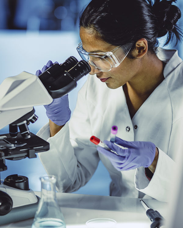 A lab technician examines a sample under a microscope