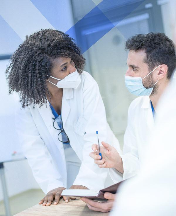 Two masked clinicians confer in a hospital setting